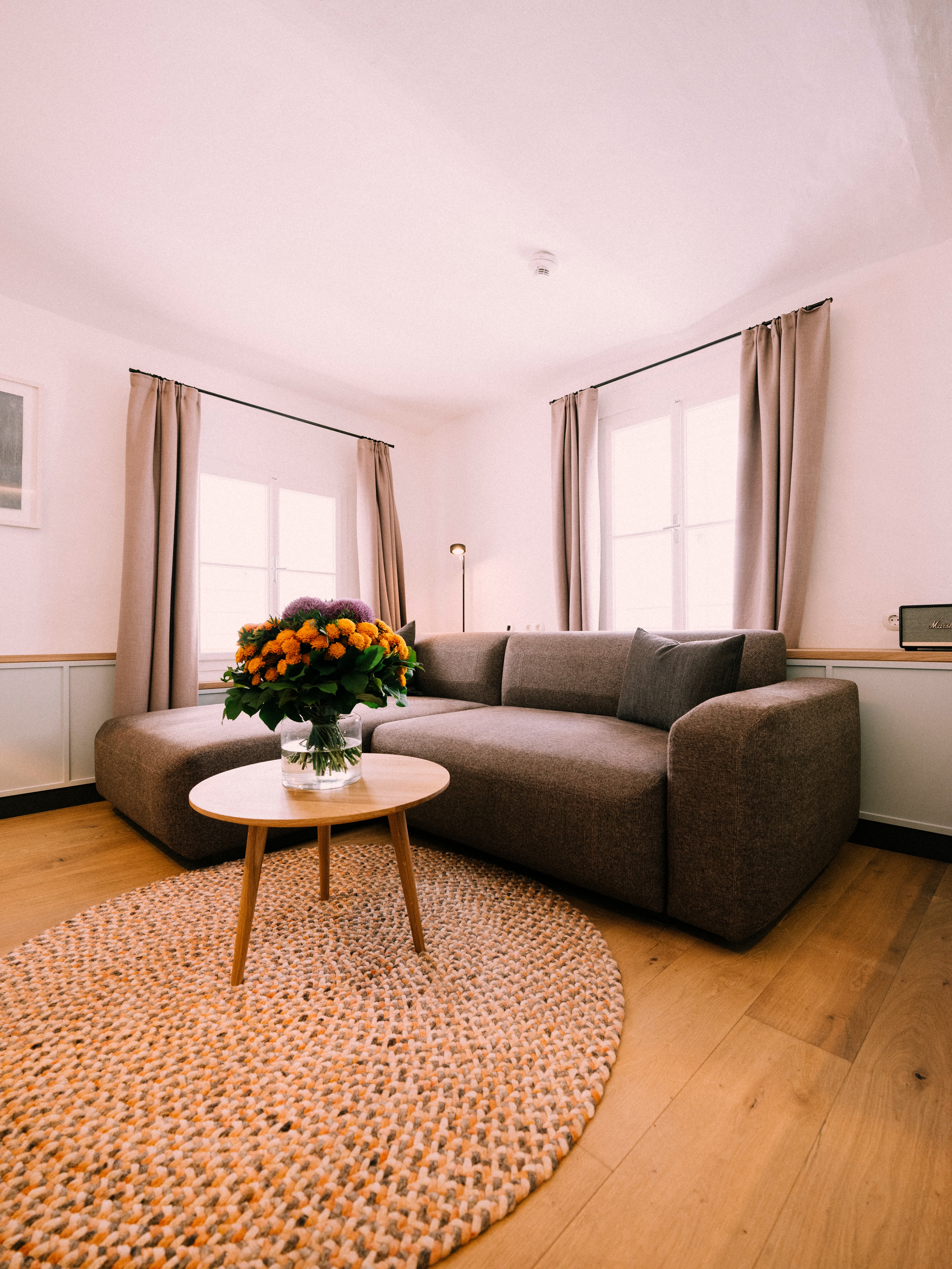 Arthotel Blaue Gans — Suite mit Loungesofa, Naturteppich und Blumen vor hellen Fenstern
